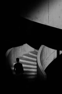 Person climbing spiral concrete staircase in abstract light and shadow (Isik tõuseb betoonist spiraaltrepil, valguse ja varju mängus)