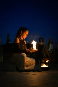 Fire artist kneeling with flames in her hands at dusk, Porto Portugal